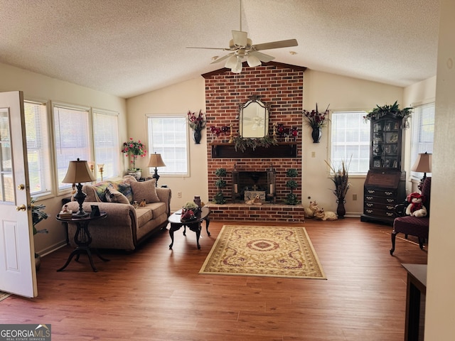 living room featuring vaulted ceiling, wood finished floors, a ceiling fan, a fireplace, and a textured ceiling