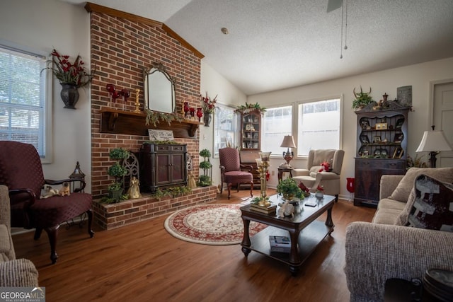 living room with a brick fireplace, hardwood / wood-style flooring, vaulted ceiling, and a textured ceiling