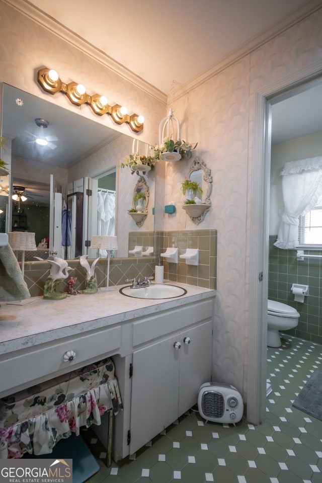 bathroom with toilet, crown molding, tile walls, vanity, and ceiling fan