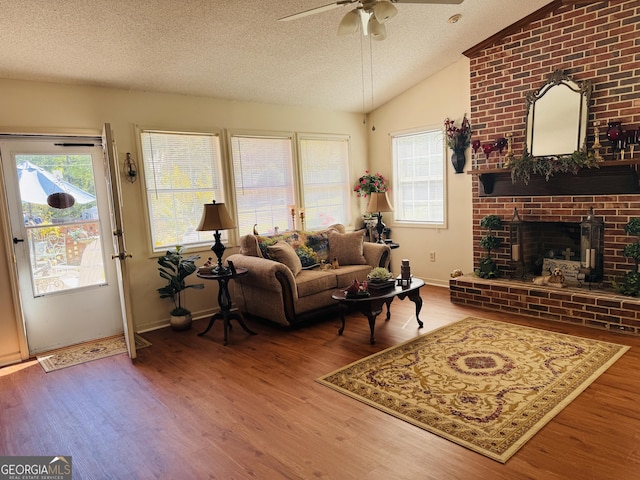 living room with vaulted ceiling, a ceiling fan, wood finished floors, a textured ceiling, and a fireplace