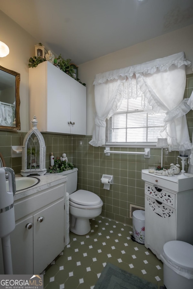 bathroom with vanity, tile patterned floors, toilet, visible vents, and tile walls