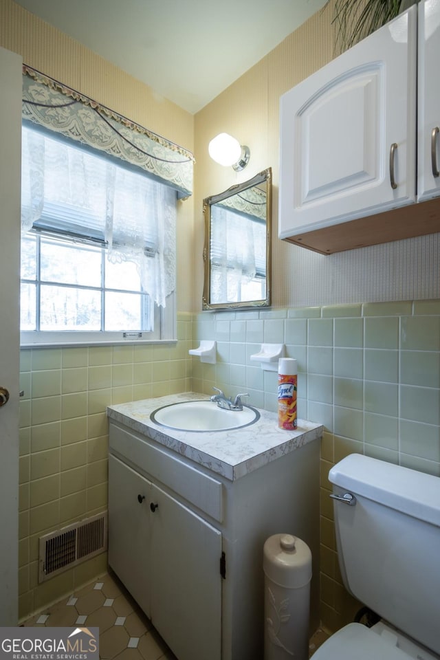 half bath with wallpapered walls, tile patterned flooring, visible vents, and tile walls