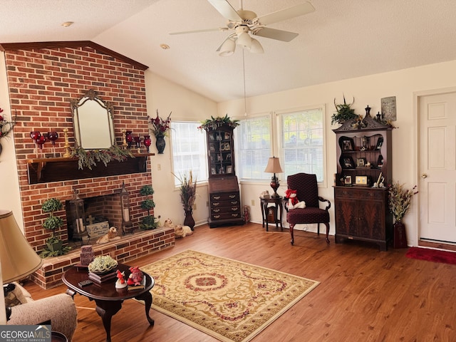 living room featuring vaulted ceiling, wood finished floors, ceiling fan, and a brick fireplace