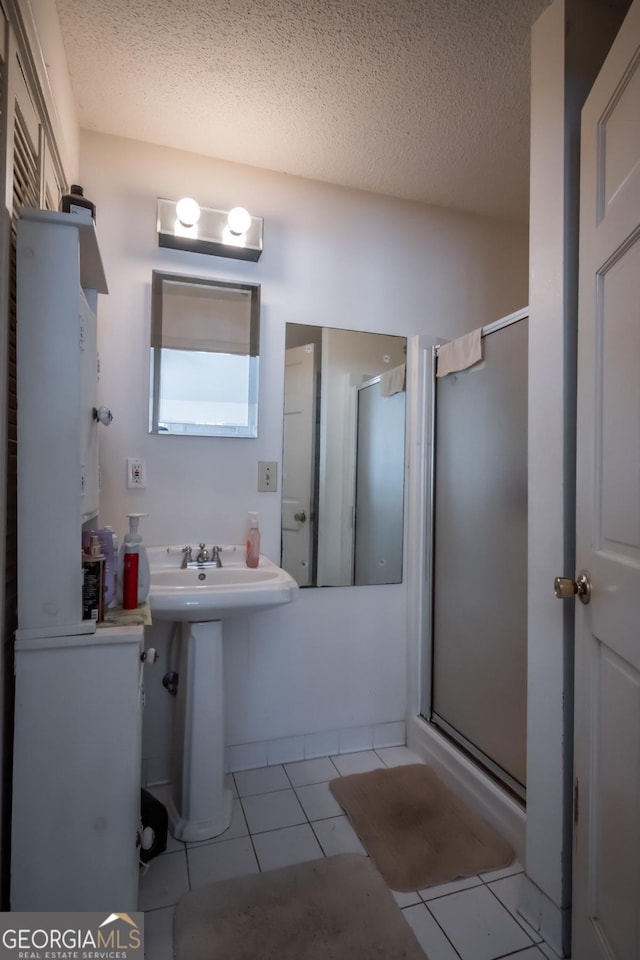 full bathroom with a shower stall, a textured ceiling, tile patterned flooring, and a sink