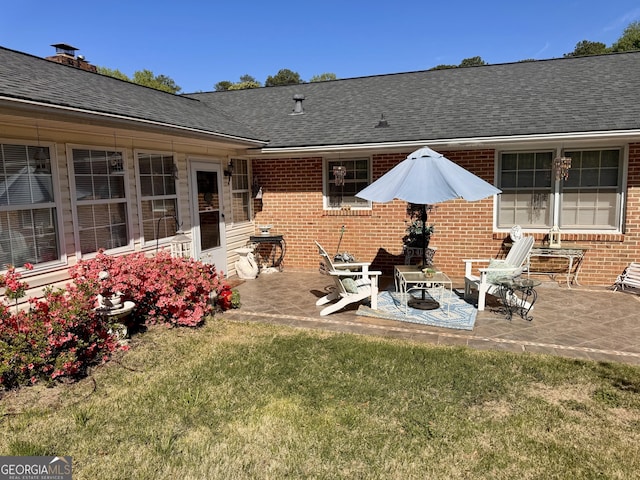 back of house featuring brick siding, a yard, a patio area, and roof with shingles
