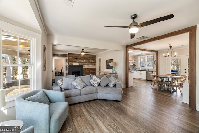 living room with sink, dark hardwood / wood-style floors, ceiling fan with notable chandelier, crown molding, and a fireplace