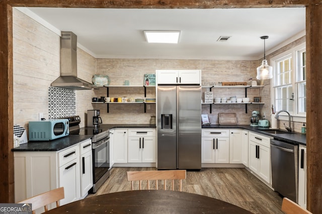 kitchen featuring sink, decorative light fixtures, wall chimney range hood, stainless steel appliances, and white cabinets