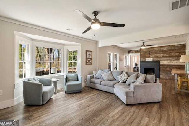 living room with ceiling fan, dark wood-type flooring, crown molding, and a brick fireplace