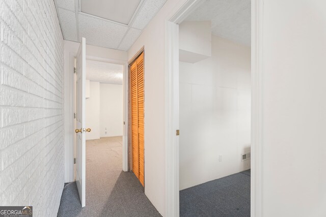 hallway with brick wall, carpet, and a drop ceiling