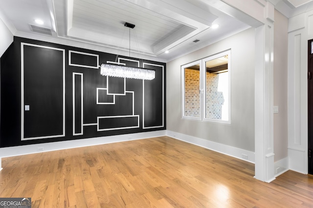 unfurnished dining area featuring wood finished floors, visible vents, baseboards, a tray ceiling, and crown molding