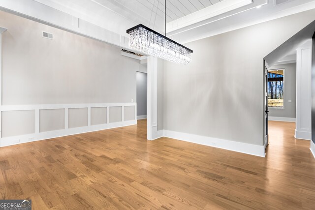 unfurnished dining area with baseboards, a notable chandelier, visible vents, and wood finished floors