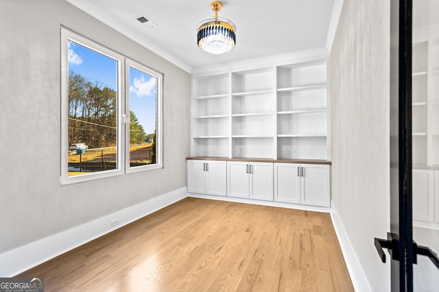 unfurnished room featuring built in shelves, light wood finished floors, visible vents, a chandelier, and baseboards