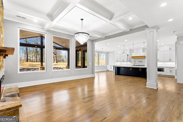 unfurnished living room with decorative columns, visible vents, wood finished floors, a stone fireplace, and a sink