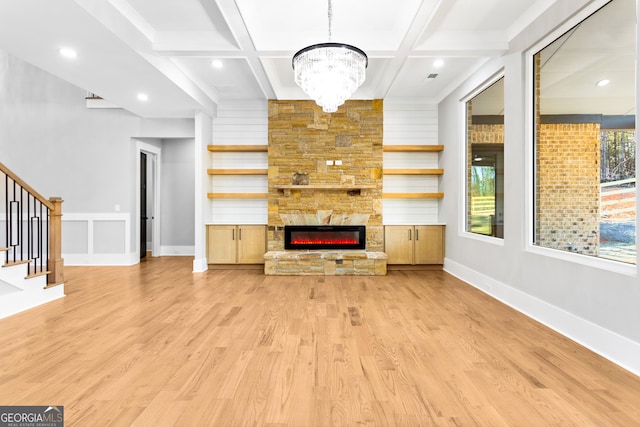 unfurnished living room with a fireplace, stairway, light wood-style floors, coffered ceiling, and beamed ceiling