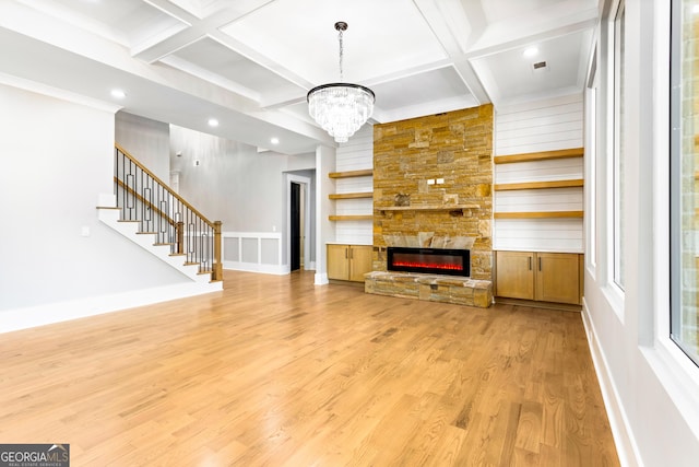 unfurnished living room featuring coffered ceiling, a fireplace, light wood finished floors, and stairs