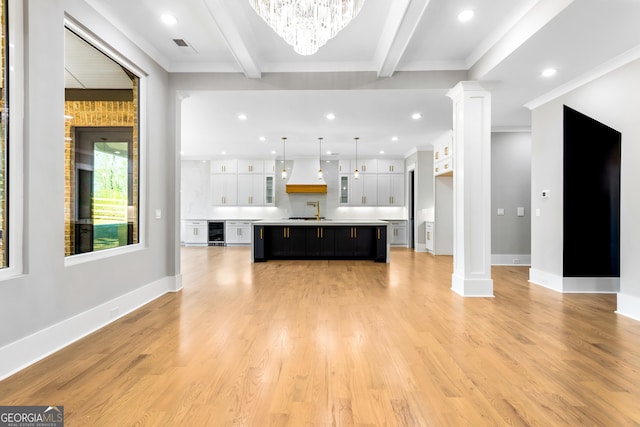 unfurnished living room with light wood-style floors, beverage cooler, decorative columns, and beamed ceiling