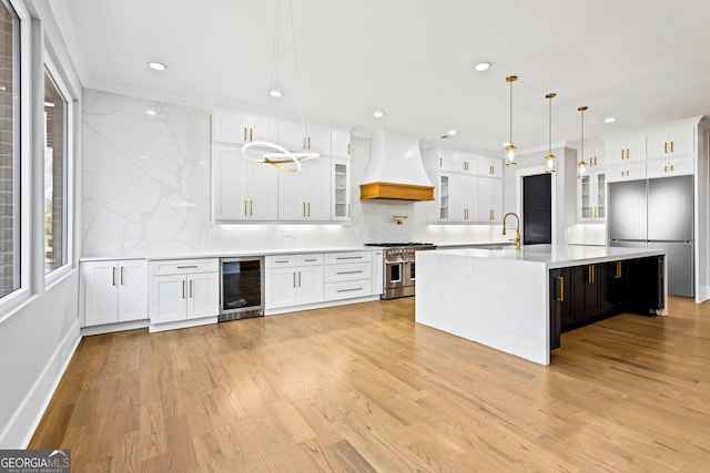 kitchen with light wood finished floors, tasteful backsplash, range with two ovens, wine cooler, and premium range hood