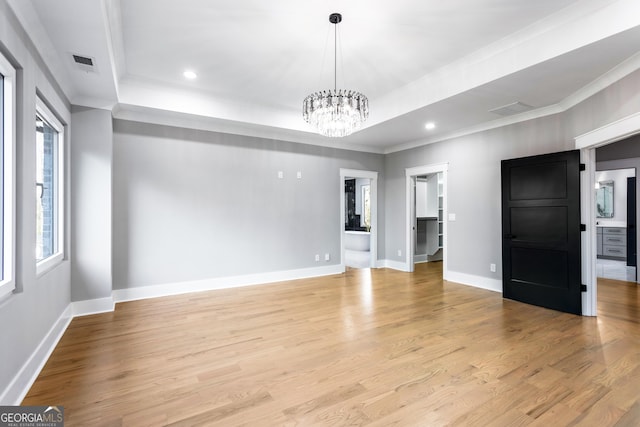 empty room with light wood-type flooring, a raised ceiling, an inviting chandelier, and baseboards