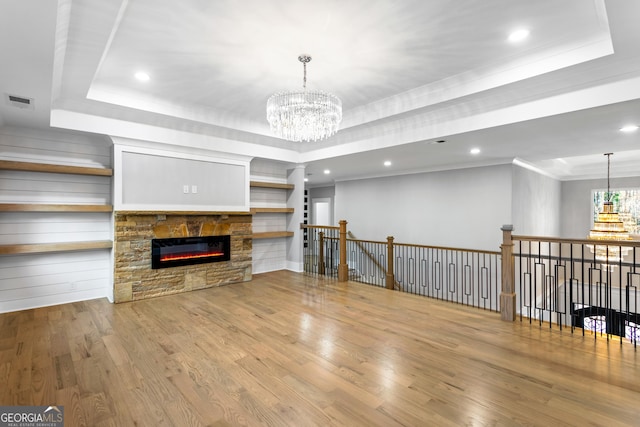 living room featuring a chandelier, a stone fireplace, wood finished floors, ornamental molding, and a tray ceiling