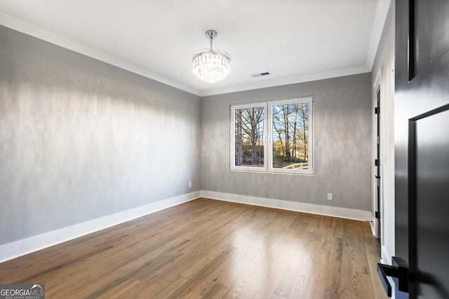 unfurnished room with crown molding, visible vents, an inviting chandelier, wood finished floors, and baseboards