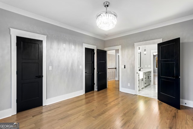 unfurnished bedroom featuring ornamental molding, light wood-type flooring, a notable chandelier, and baseboards