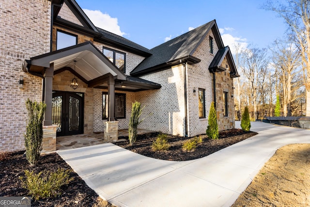 view of exterior entry featuring french doors, brick siding, and fence