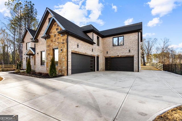 view of side of home featuring driveway, a garage, stone siding, fence, and brick siding