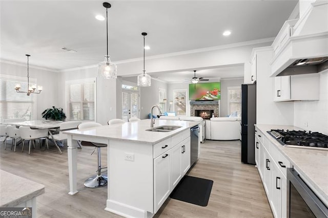 kitchen with appliances with stainless steel finishes, sink, custom exhaust hood, hanging light fixtures, and a kitchen island with sink