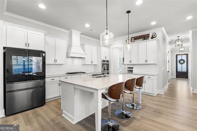 kitchen featuring a center island with sink, appliances with stainless steel finishes, custom exhaust hood, white cabinetry, and pendant lighting