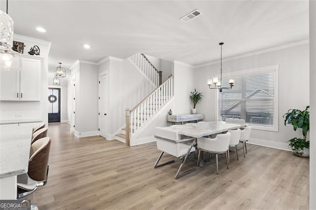 dining space with light wood-type flooring, ornamental molding, and a notable chandelier