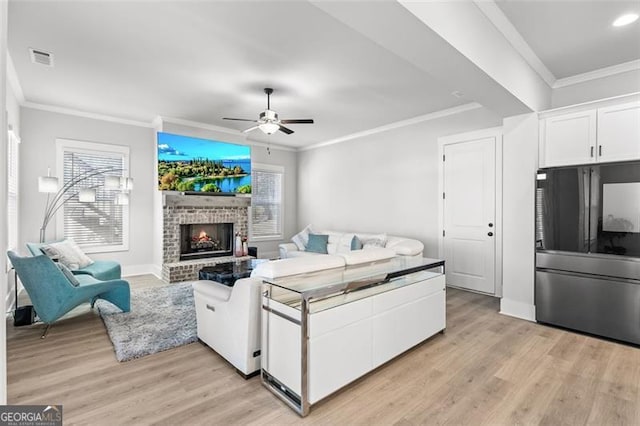 living room with ceiling fan, a brick fireplace, crown molding, and light hardwood / wood-style floors