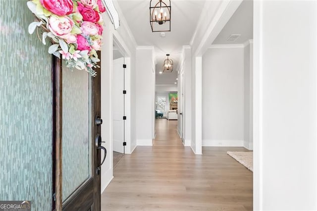 foyer with ornamental molding, light wood-type flooring, and a chandelier