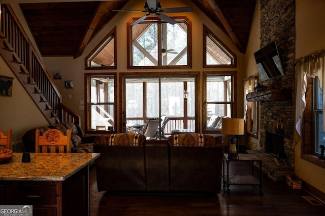 living room featuring a stone fireplace, plenty of natural light, vaulted ceiling with beams, and ceiling fan