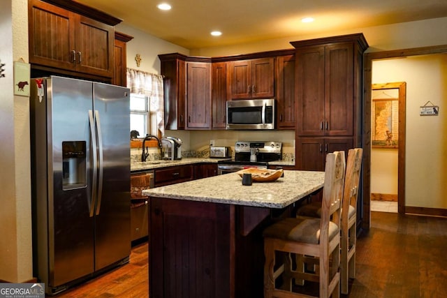 kitchen featuring sink, stainless steel appliances, a center island, light stone counters, and dark hardwood / wood-style flooring