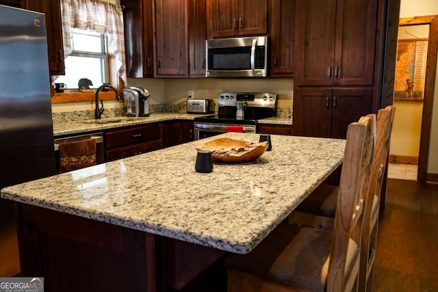 kitchen featuring light stone counters, sink, a kitchen bar, and appliances with stainless steel finishes