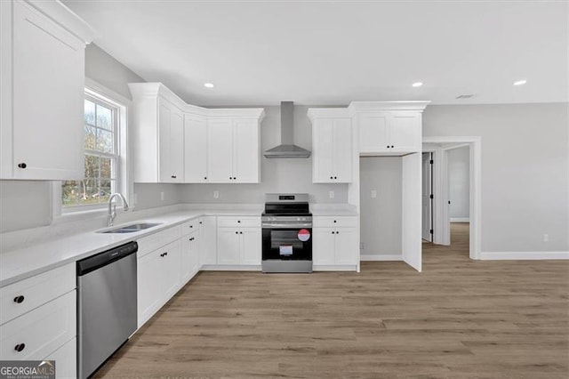 kitchen with stainless steel appliances, white cabinetry, sink, and wall chimney range hood