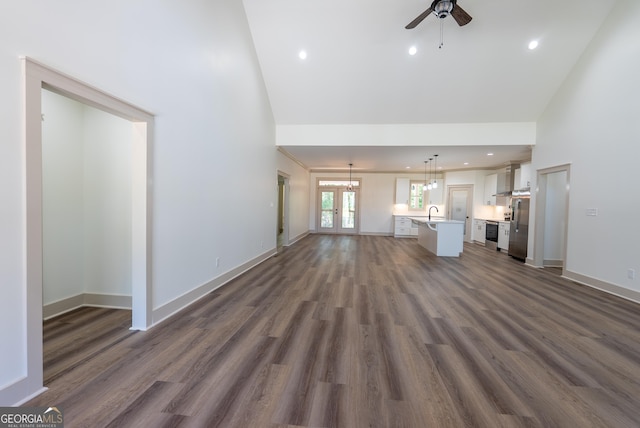 unfurnished living room with high vaulted ceiling, ceiling fan, a chandelier, dark wood-style floors, and baseboards