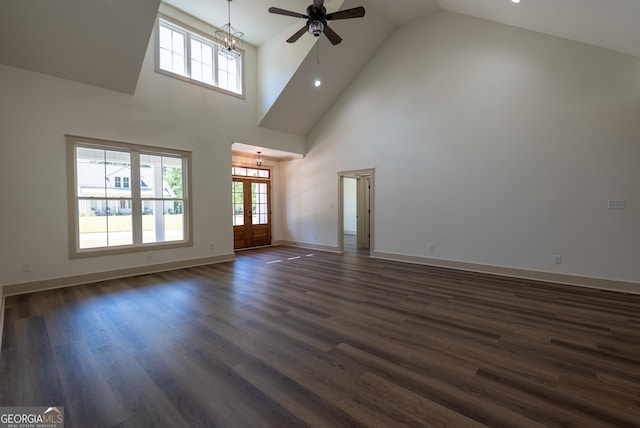 unfurnished living room with a chandelier, ceiling fan, high vaulted ceiling, dark wood-type flooring, and baseboards