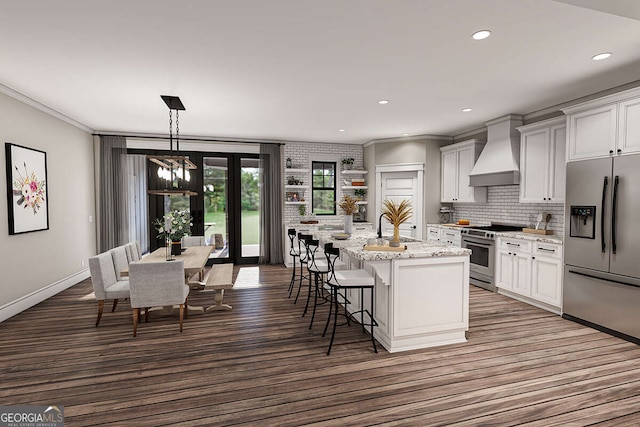 kitchen with tasteful backsplash, premium range hood, a center island with sink, a breakfast bar, and stainless steel appliances