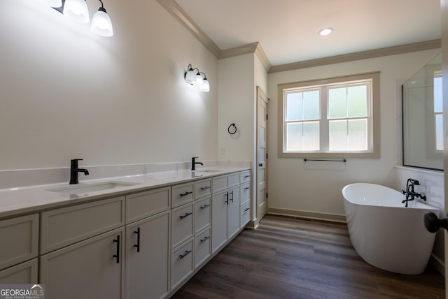 bathroom featuring crown molding, baseboards, a freestanding bath, wood finished floors, and double vanity