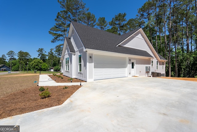view of home's exterior with board and batten siding, a shingled roof, a garage, driveway, and central air condition unit