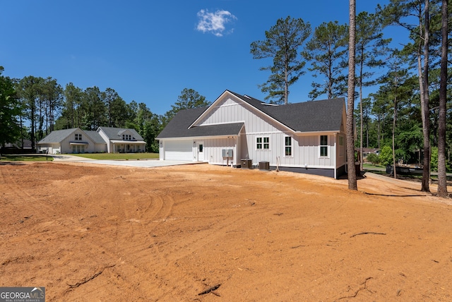 view of front of home featuring board and batten siding, an attached garage, driveway, roof with shingles, and cooling unit