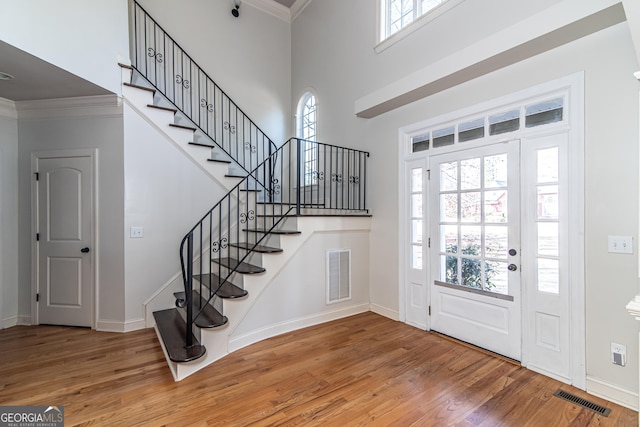 foyer entrance featuring a towering ceiling, ornamental molding, and wood-type flooring