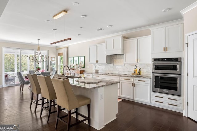 kitchen with pendant lighting, sink, white cabinets, and a center island with sink