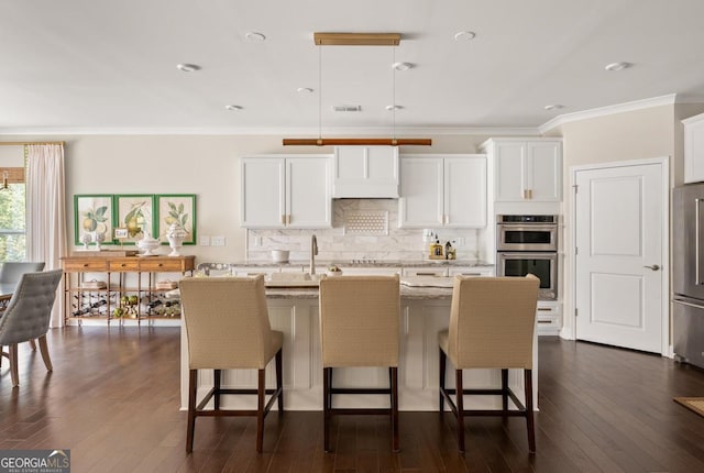 kitchen featuring pendant lighting, white cabinetry, light stone counters, stainless steel appliances, and a center island with sink