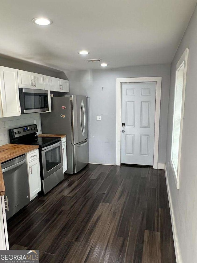 kitchen featuring wood counters, dark hardwood / wood-style flooring, white cabinets, stainless steel appliances, and backsplash