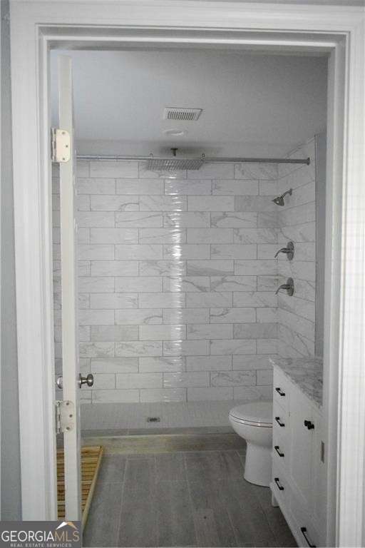 bathroom featuring hardwood / wood-style flooring, vanity, tiled shower, and toilet