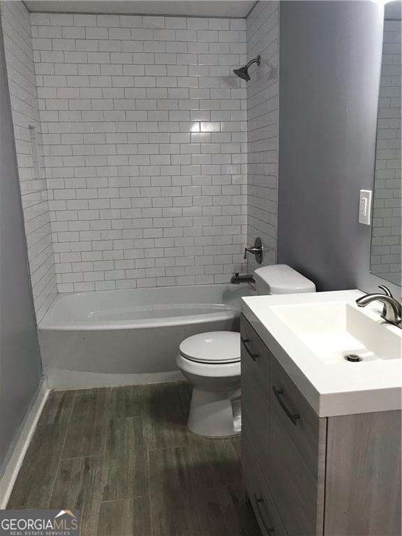 full bathroom featuring hardwood / wood-style flooring, vanity, tiled shower / bath combo, and toilet