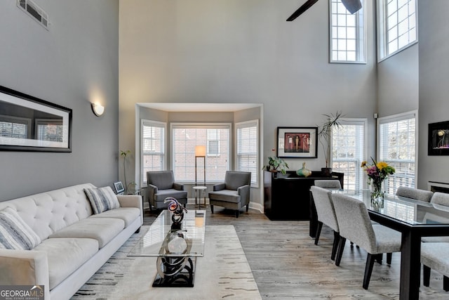 living room featuring light wood-style floors, a high ceiling, and visible vents