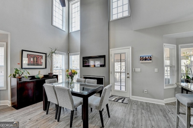 dining area with a towering ceiling, light wood-style floors, and baseboards